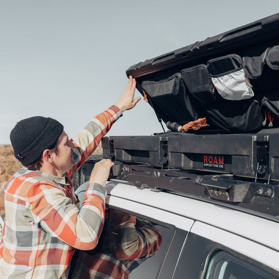 Man using the lid organizer of a low-profile 83L Rugged Case mounted on top of a vehicle